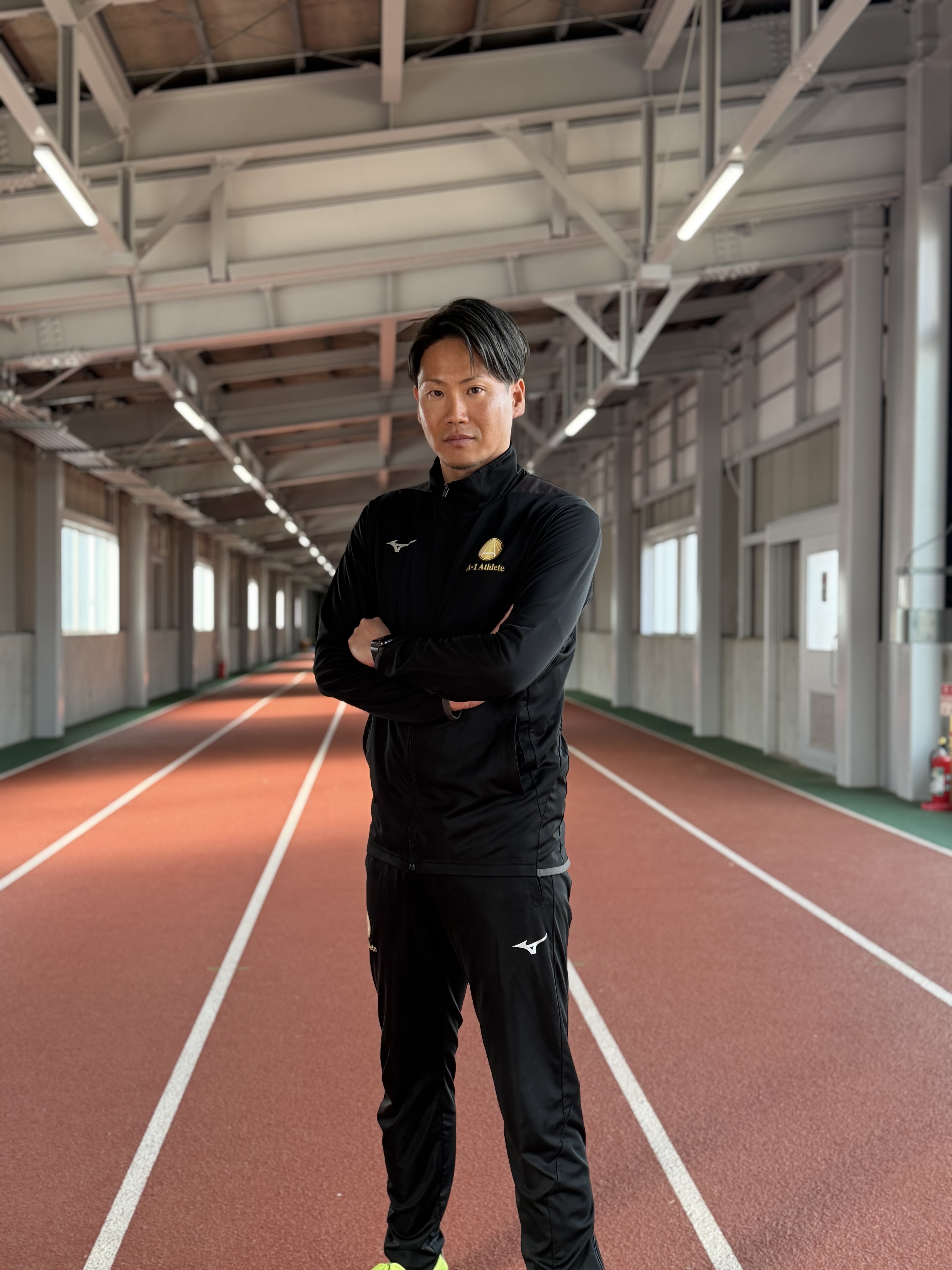 屋内トラックで腕を組んで立つ講師のポートレート